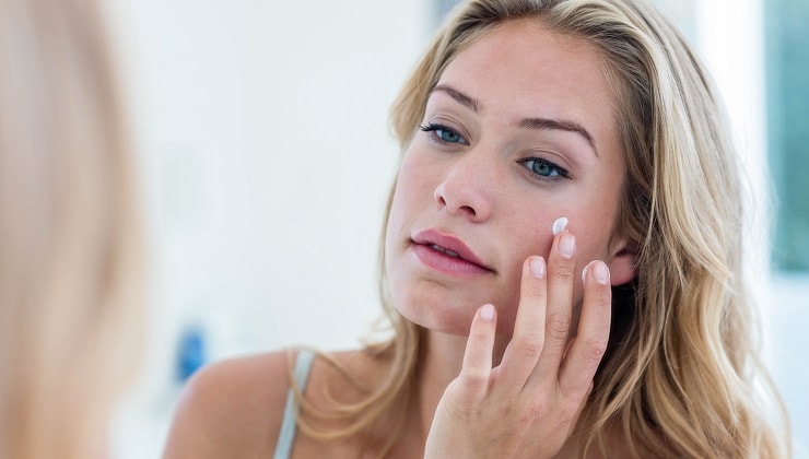 blonde woman applies cream on her face